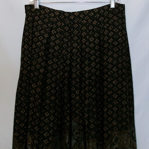 May include: A long, dark skirt with a repeating floral pattern in shades of brown and gold against a black background. The skirt is hanging on a metal hanger, showcasing its full length and design. The fabric appears lightweight.