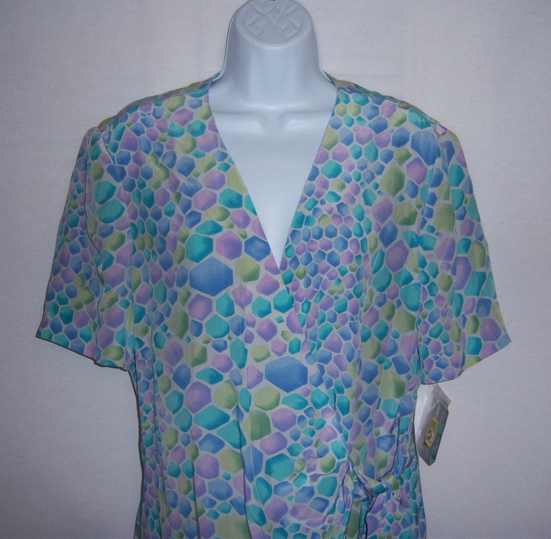 May include: A short-sleeved wrap top in a pastel geometric pattern of blue, green, and purple. The top has a V-neck and a tie closure at the waist. The fabric appears to be lightweight and suitable for warm weather.