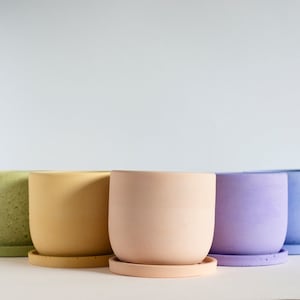 May include: Five colorful, round ceramic planters with matching saucers. The planters are in shades of green, yellow, peach, lavender, and blue. The pots have a smooth, matte finish and are suitable for indoor or outdoor use.