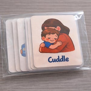 May include: A pack of illustrated cards in a clear plastic sleeve. The cards show a cartoon image of a mother hugging a child, with the word "Cuddle" in blue. The mother is wearing a red top.