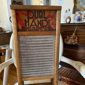 Op de afbeelding: Vintage houten wasbord met een gegolfd metalen oppervlak. Het wasbord heeft een rood en zwart label met de tekst "Duble Handi" en "Columbus Washboard Co. Columbus, O."