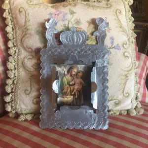 May include: A silver metal picture frame with a scalloped edge and a raised design of a pumpkin and two birds. The frame holds a religious image of Saint Joseph holding a baby Jesus.