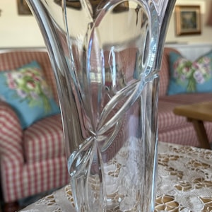 Könnte beinhalten: Eine klare Glasvase mit einem geschliffenen Glasdesign. Die Vase hat eine breite Öffnung und einen schmalen Boden.