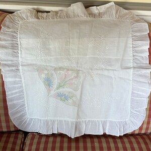 Könnte beinhalten: Ein weißes Kissen mit einem zarten floralen Stickmuster. Das Kissen hat einen Rüschenrand und liegt auf einem rot-weiß gestreiften Sofa.