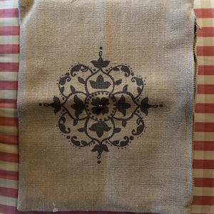 May include: A brown burlap pillow with a black and white floral design. The pillow has a zipper closure.