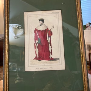 May include: A framed antique print of a man in a red robe and white collar, holding a book. The print is titled "Premier President au parlement de Paris" and is in a gold frame with a green mat.