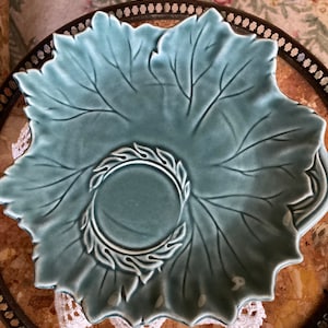 May include: A teal blue ceramic dish shaped like a leaf with a raised design of a wreath in the center.