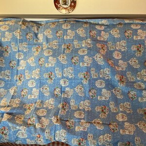 May include: A light blue fabric with a repeating pattern of white floral arrangements. The floral arrangements are in white vases with red, pink, and green flowers. The fabric is likely used for bedding or curtains.