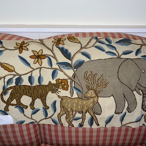 May include: A cream-colored pillow with an embroidered design of a tiger, deer, and elephant in a jungle setting. The pillow has a blue, brown, and yellow color scheme.