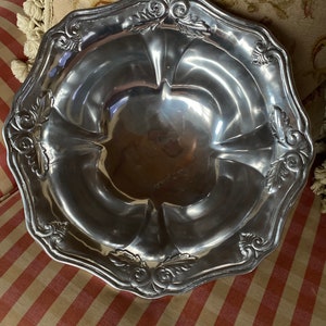 May include: A silver serving bowl with a scalloped edge and ornate floral designs. The bowl is made of metal and has a shiny finish.