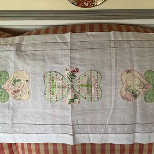 May include: White linen table runner with embroidered green bows and pink and green floral designs.