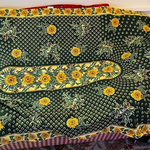 May include: A green tablecloth with a yellow sunflower pattern. The tablecloth has a scalloped edge and a center oval with a sunflower design.