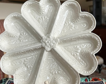 May include: White ceramic serving dish with six heart-shaped compartments and intricate floral designs. The dish is on a white metal stand with ornate details.