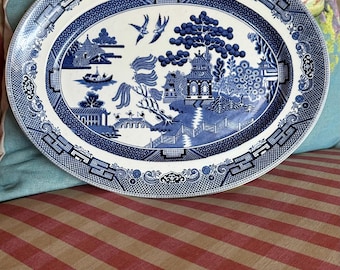 Op de afbeelding: Een ovale serveerschaal met een traditioneel wilgenmotief in blauw en wit. De schaal heeft een gestileerde wilgenboom, een pagode en een brug.