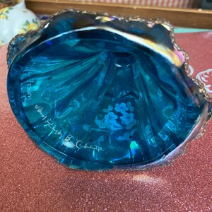 May include: A blue glass bowl with a scalloped edge and a floral design. The bowl is signed "Mary  B.  Cabot" and "Preston,  Shenandoah,  VA".