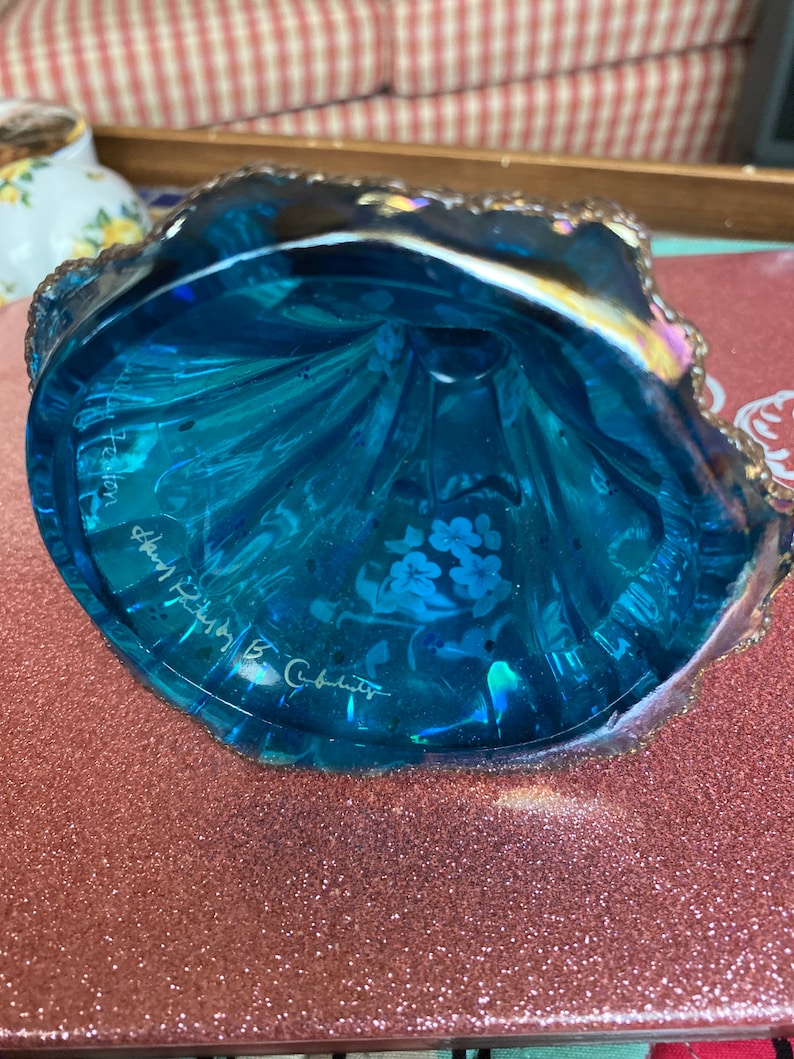 May include: A blue glass bowl with a scalloped edge and a floral design. The bowl is signed "Mary  B.  Cabot" and "Preston,  Shenandoah,  VA".