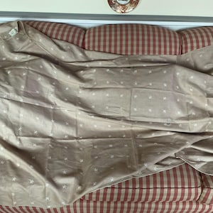 May include: A tan fabric with a repeating white floral pattern is draped over a red and white striped couch. The fabric is folded and appears to be a sheet or tablecloth. The couch has a rounded back.
