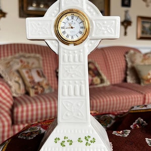Peut inclure: Horloge en forme de croix celtique en porcelaine blanche avec des accents dorés et des trèfles verts. Le cadran de l'horloge a des chiffres romains et un cadre doré.