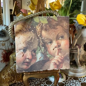 Peut inclure: Une œuvre d'art encadrée de style vintage représentant deux enfants ressemblant à des chérubins, l'un avec un doigt sur les lèvres, l'autre avec une expression sérieuse. L'œuvre d'art a un aspect vieilli et détérioré et est encadrée d'une bordure en corde.