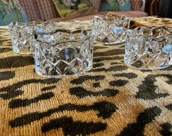 May include: Five clear crystal votive candle holders with a diamond pattern and scalloped edges. Each holder has a blue and white label that reads "GORHAM". The candle holders are on a patterned surface.