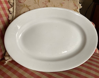 May include: A large, white oval serving platter with a slightly raised rim. The platter is made of ceramic and has a smooth, glossy finish.