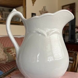 以下が含まれることがあります： 波打つ縁と取っ手のある白い陶器のピッチャー。ピッチャーは洋梨の形をしたボディと滑らかで光沢のある仕上げをしています。