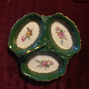 May include: A green and gold three-section serving dish with a handle. Each section features a floral design in white.