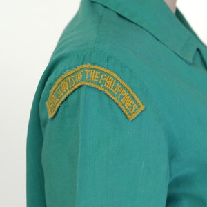 K&ouml;nnte beinhalten: Ein gr&uuml;nes Uniformhemd mit einem gestickten gelben Aufn&auml;her mit der Aufschrift "Girl Scouts of the Philippines".