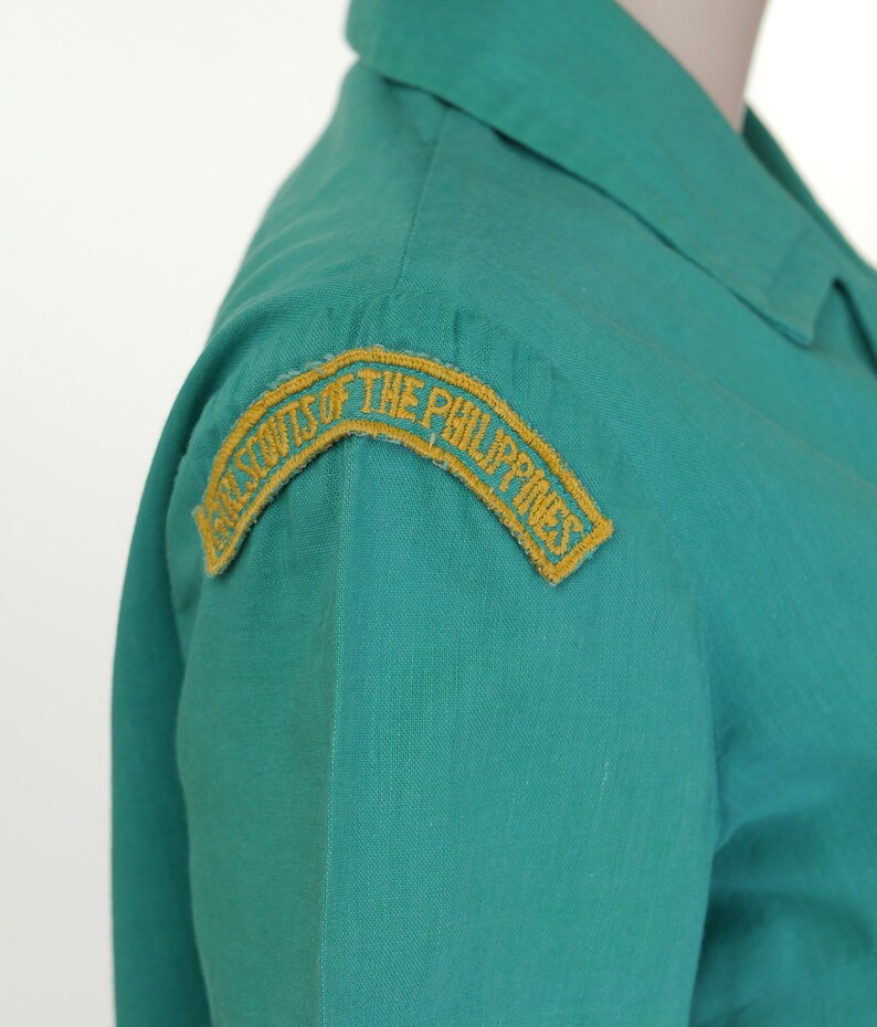 K&ouml;nnte beinhalten: Ein gr&uuml;nes Uniformhemd mit einem gestickten gelben Aufn&auml;her mit der Aufschrift "Girl Scouts of the Philippines".