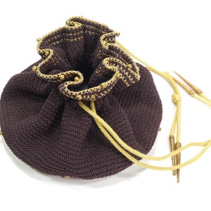 May include: A brown crocheted drawstring bag with gold trim and beads. The bag has two long, yellow cords with gold tips.