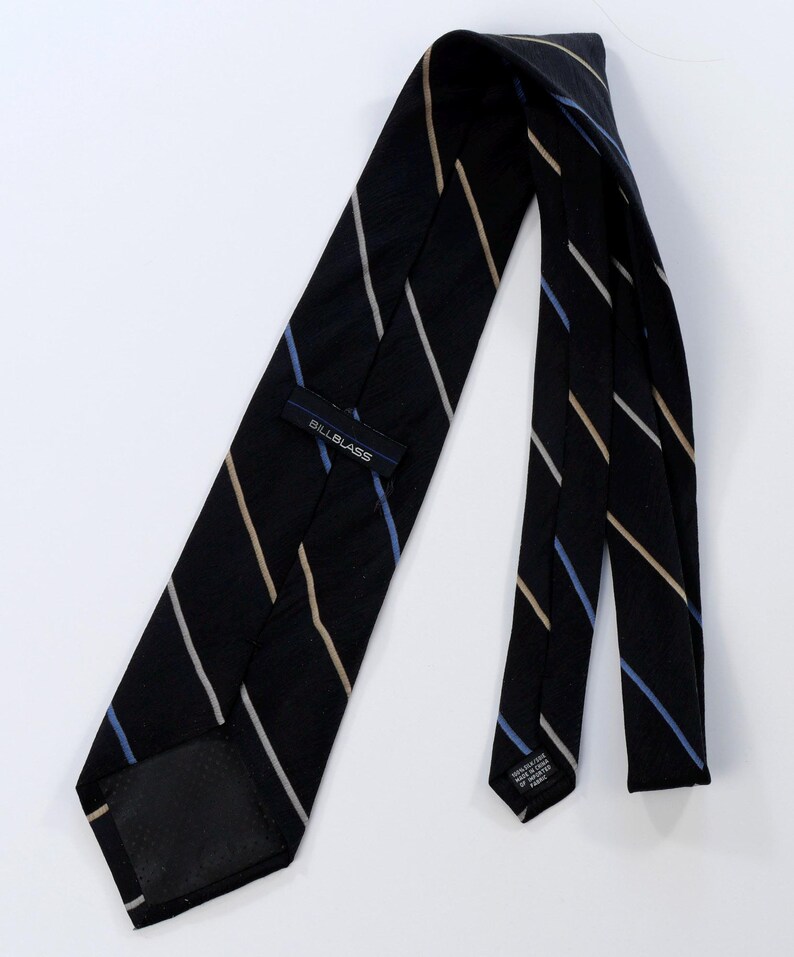 Puede incluir: Una corbata negra con rayas diagonales blancas, beige y azules. La etiqueta dice "BILLBLASS". La corbata es de seda, un accesorio cl&aacute;sico.