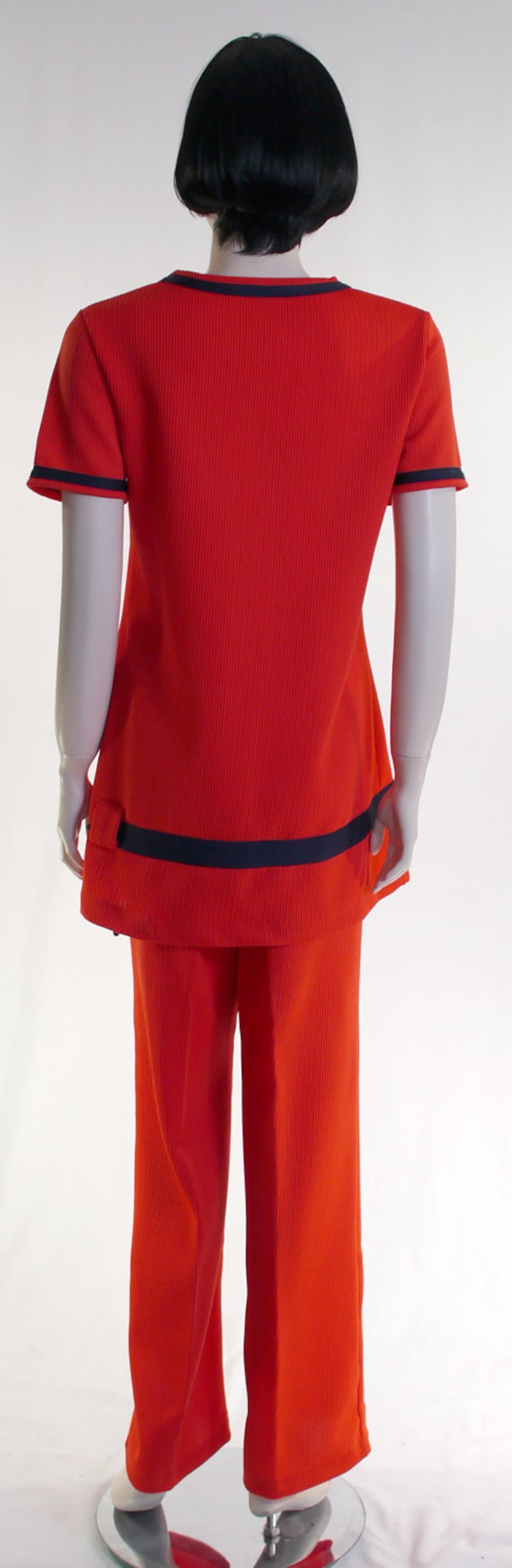 May include: A red ribbed knit jumpsuit with black trim on the sleeves and waist. The jumpsuit has a wide-leg style.