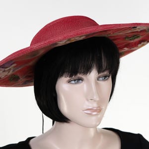 May include: A wide-brimmed red hat with a floral print. The hat has a wide, flat brim and a low crown.