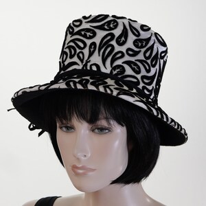 May include: A black and white hat with a paisley pattern. The hat has a wide brim and a tall crown.