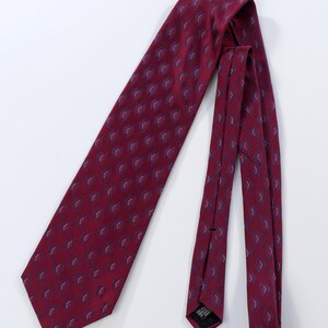 Puede incluir: Una corbata burdeos con un patr&oacute;n repetitivo de peque&ntilde;os dise&ntilde;os en forma de diamante en azul y blanco. La corbata est&aacute; hecha de una tela suave y se muestra sobre un fondo blanco. Un accesorio cl&aacute;sico.