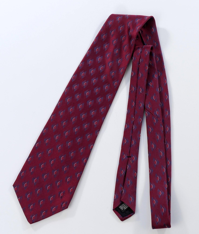 Puede incluir: Una corbata burdeos con un patr&oacute;n repetitivo de peque&ntilde;os dise&ntilde;os en forma de diamante en azul y blanco. La corbata est&aacute; hecha de una tela suave y se muestra sobre un fondo blanco. Un accesorio cl&aacute;sico.