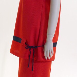 May include: A red ribbed knit jumpsuit with a navy blue trim and a tie at the waist.