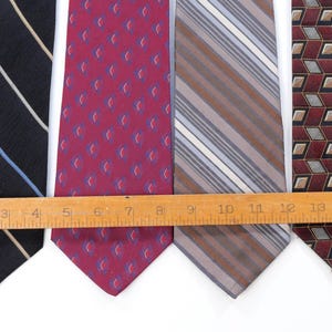 Puede incluir: Se muestran cuatro corbatas de varios patrones y colores. Las corbatas incluyen una corbata azul marino con rayas blancas y celeste, una corbata burdeos con un patr&oacute;n repetido, una corbata a rayas y una corbata con estampado geom&eacute;trico. Una regla de madera se coloca sobre las corbatas.