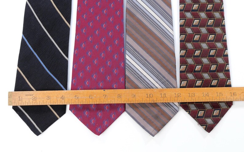 Puede incluir: Se muestran cuatro corbatas de varios patrones y colores. Las corbatas incluyen una corbata azul marino con rayas blancas y celeste, una corbata burdeos con un patr&oacute;n repetido, una corbata a rayas y una corbata con estampado geom&eacute;trico. Una regla de madera se coloca sobre las corbatas.