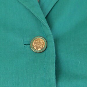 K&ouml;nnte beinhalten: Ein blauer Blazer mit einem goldenen Knopf mit einem Design.