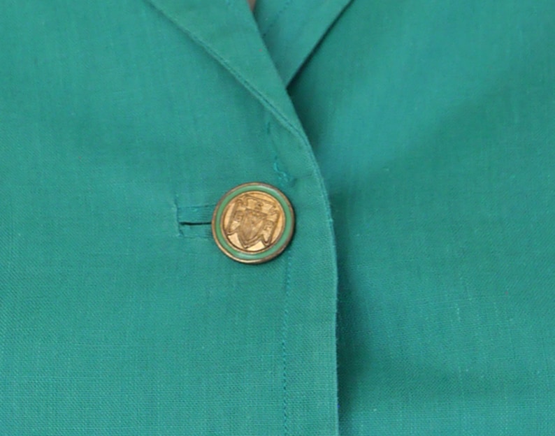 K&ouml;nnte beinhalten: Ein blauer Blazer mit einem goldenen Knopf mit einem Design.