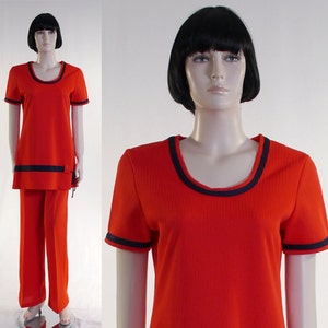 May include: A red ribbed knit jumpsuit with black trim around the neckline and sleeves. The jumpsuit has a scoop neckline and short sleeves.
