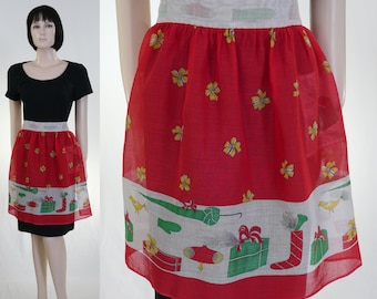 May include: A red and white Christmas-themed apron with a white waistband and a red skirt featuring yellow flowers and a white border with a green and red Christmas design.