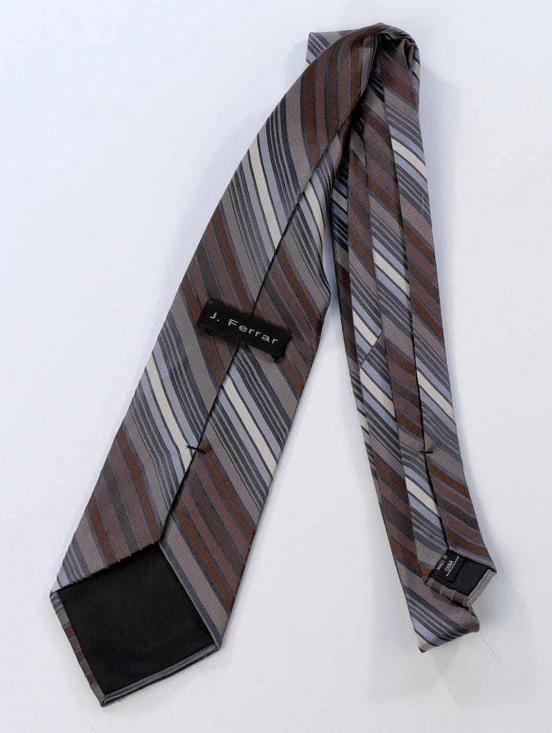 Puede incluir: Corbata a rayas marrones, grises y blancas con la etiqueta "J. Ferrar". La corbata es de tejido liso y est&aacute; en &aacute;ngulo sobre un fondo blanco. Las rayas son diagonales.