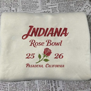 Könnte beinhalten: Cremefarbenes besticktes Sweatshirt mit dem Text "INDIANA Rose Bowl 25 26 PASADENA, CALIFORNIA" in Rot und Grün. Mit einem Rosendesign.