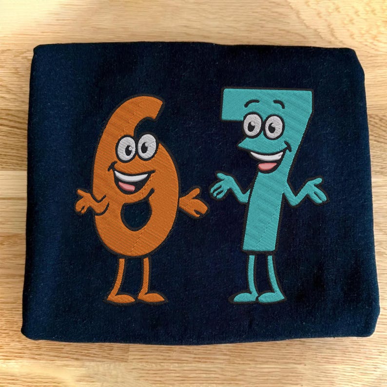 K&ouml;nnte beinhalten: Marineblauer Stoff mit gestickten Cartoon-Zahlen sechs und sieben. Die Zahl sechs ist orange und die Zahl sieben ist t&uuml;rkis. Beide Zahlen haben l&auml;chelnde Gesichter, Arme und Beine.