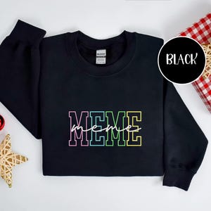 May include: Black sweatshirt with the word "MEME" in a colorful, outlined font across the chest. The word "meme" is written in a cursive font over the word "MEME". A black circle with the word "BLACK" is in the upper right corner.