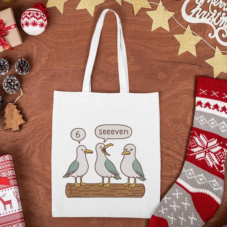 May include: White tote bag featuring a cartoon illustration of three seagulls perched on a log. One seagull is speaking, with the text "6" and "See even" in speech bubbles. The bag has two white handles.