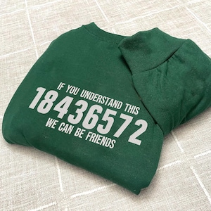 May include: A dark green sweatshirt with the text "IF YOU UNDERSTAND THIS 18436572 WE CAN BE FRIENDS" printed in white. The sweatshirt is folded, showing the crew neck and a portion of the sleeve.