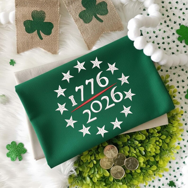May include: A green fabric item with the numbers "1776" and "2026" in white, encircled by white stars, and a red line. The item is on a white surface with shamrock decorations and gold coins.